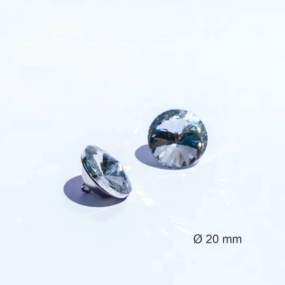 Botón acrílico BTN0620, 20 mm., 50 unds.-BOTONES-Botones de Tapicería de Cristal con Engarce Metálico Eleva la estética de tus muebles tapizados con estos exquisitos botones de cristal. Diseñados para añadir un toque de lujo y sofisticación, estos botones cuentan con un cristal facetado que captura y refleja la luz, creando un efecto brillante y llamativo. Cada botón está engarzado en una base metálica. La parte trasera del botón incorpora un asa metálica, facilitando su fijación en la tapicería y garantiza
