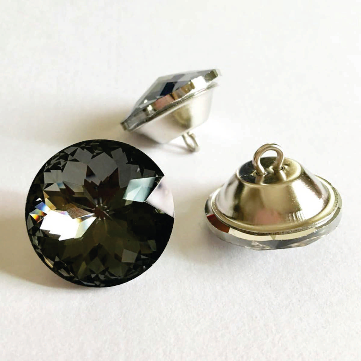 Botón acrílico BTN0620G, 20 mm., 50 unds.-BOTONES-Botones de Tapicería de Cristal con Engarce Metálico Eleva la estética de tus muebles tapizados con estos exquisitos botones de cristal. Diseñados para añadir un toque de lujo y sofisticación, estos botones cuentan con un cristal facetado que captura y refleja la luz, creando un efecto brillante y llamativo. Cada botón está engarzado en una base metálica. La parte trasera del botón incorpora un asa metálica, facilitando su fijación en la tapicería y garantiz