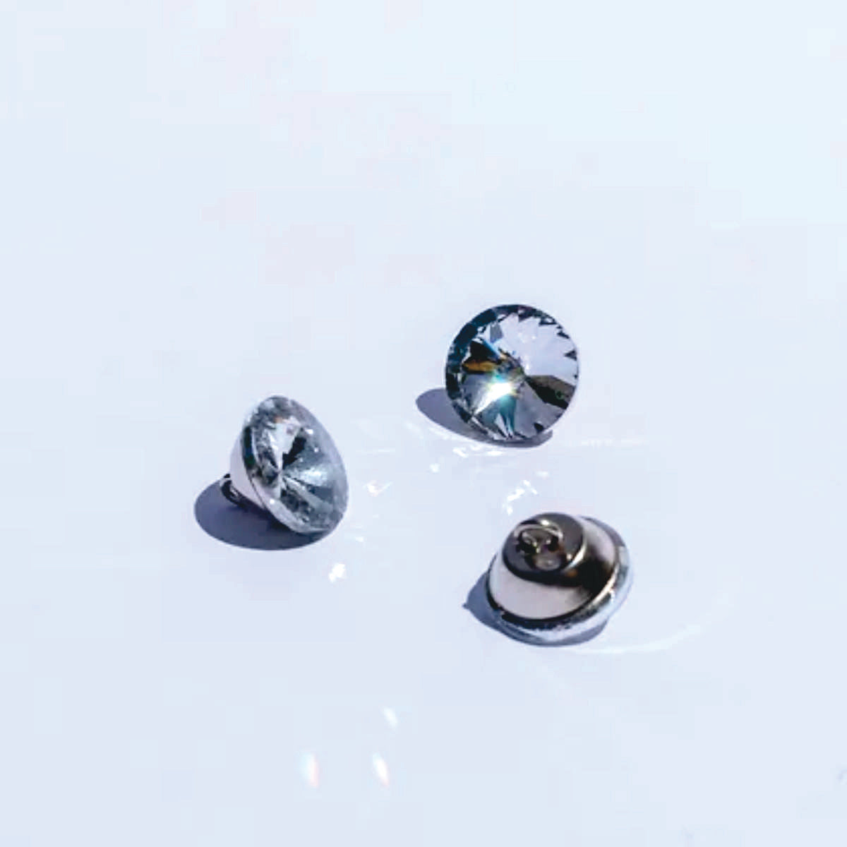 Botón acrílico BTN0620, 20 mm., 50 unds.-BOTONES-Botones de Tapicería de Cristal con Engarce Metálico Eleva la estética de tus muebles tapizados con estos exquisitos botones de cristal. Diseñados para añadir un toque de lujo y sofisticación, estos botones cuentan con un cristal facetado que captura y refleja la luz, creando un efecto brillante y llamativo. Cada botón está engarzado en una base metálica. La parte trasera del botón incorpora un asa metálica, facilitando su fijación en la tapicería y garantiza